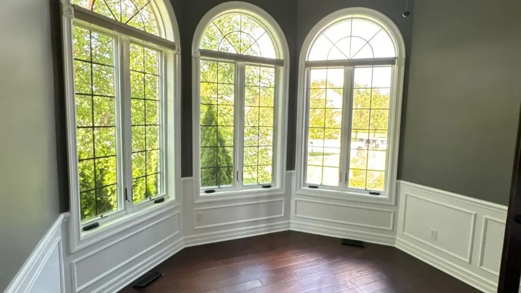 Bay window nook with dark gray walls above white paneled wainscoting and dark wood floors
